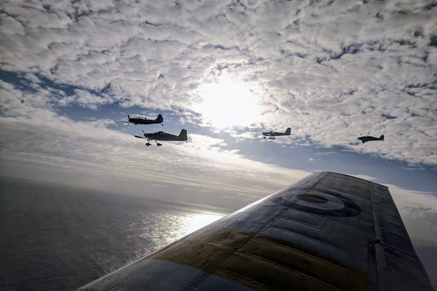 A view over the wing of a plane in the air of four other planes in formation.