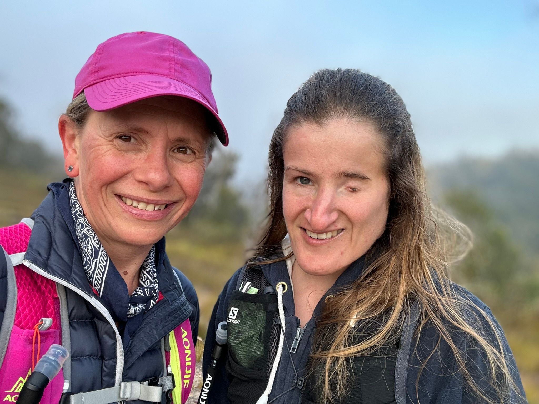 Two smiling women on a bushy slope.