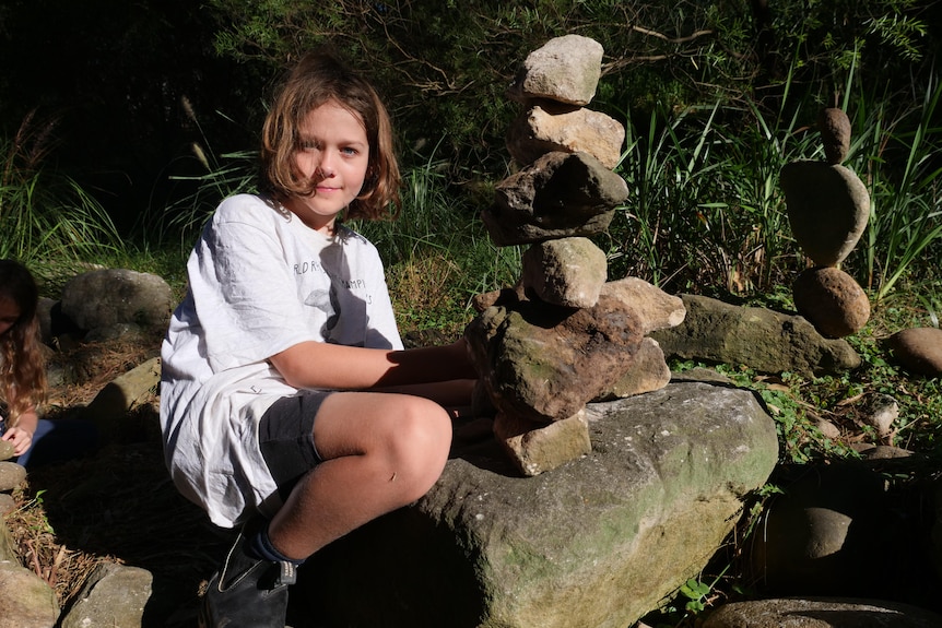 A boy squats next to a pile of rocks. 