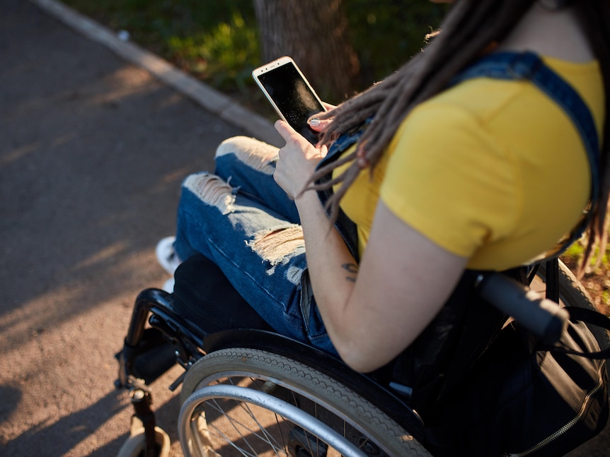 A woman in a wheelchair outdoors using a smartphone
