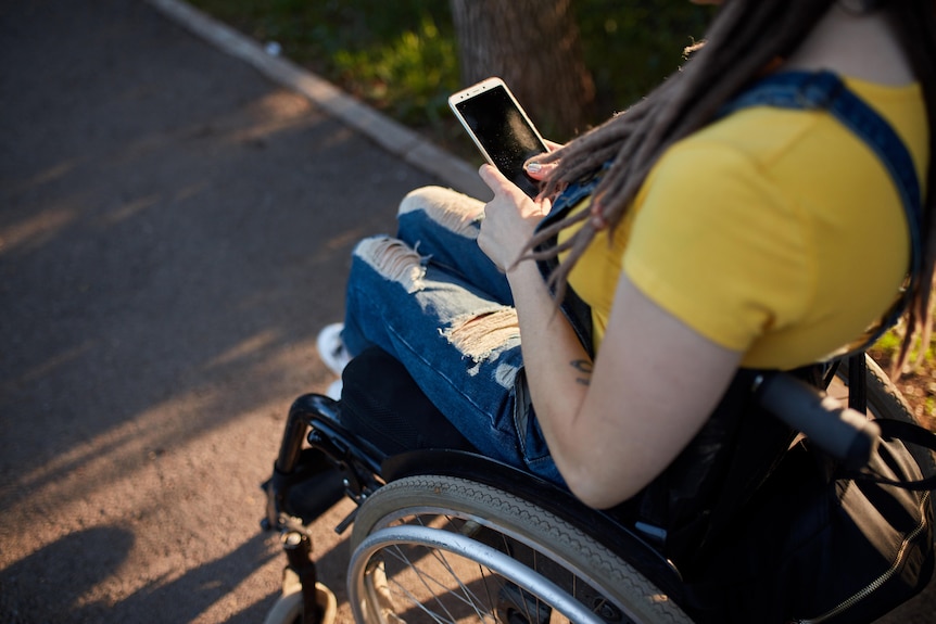 A woman in a wheelchair outdoors using a smartphone