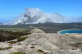 A bushfire and smoke seen in the distance from the top of a mountain on an island.