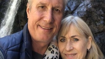 A man and woman in a selfie in front of a waterfall.