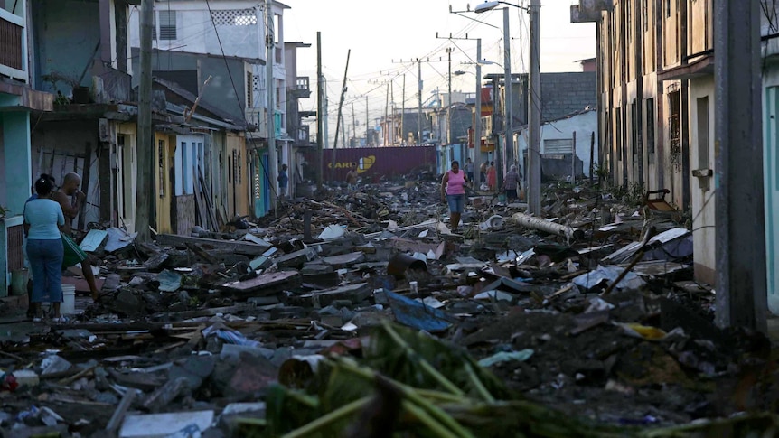 A woman walks along a street covered in debris in Baracoa, Cuba.