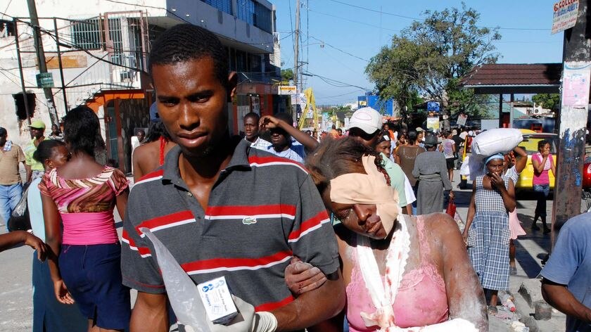 An injured woman is helped down a street after being rescued in Port-au-Prince