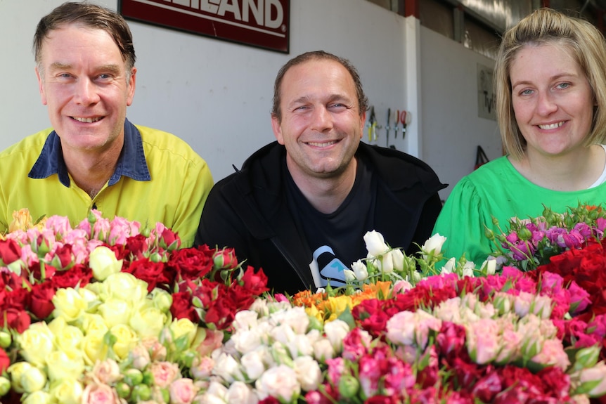 three people stand in front of bunches of colourful roses