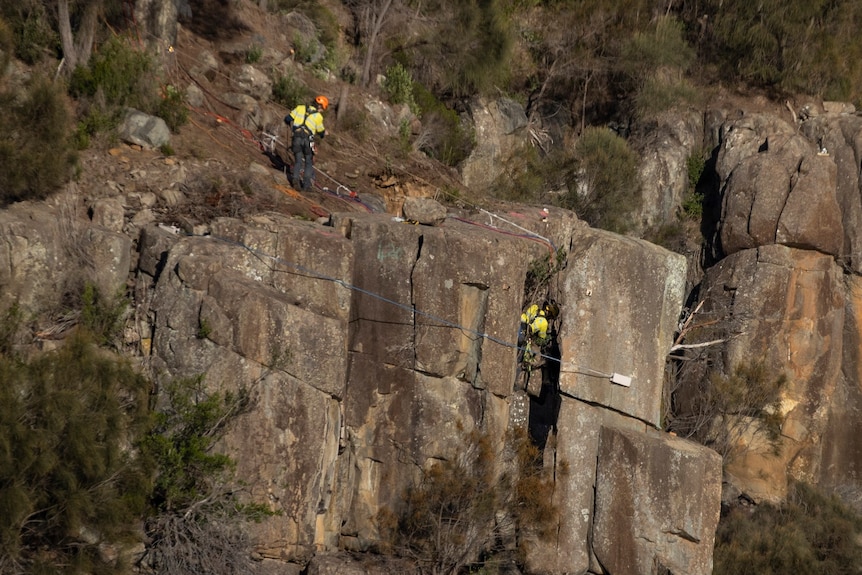 Two workers attending a rock face in the bush.
