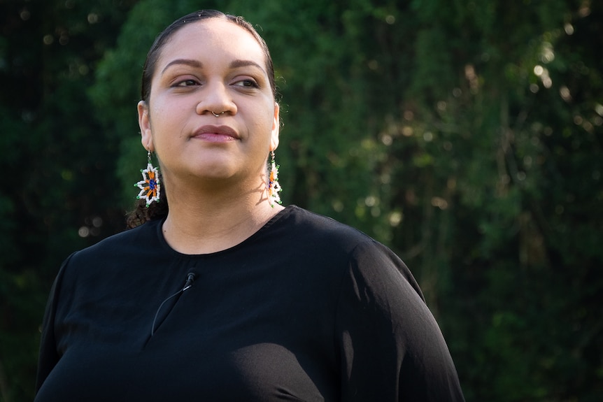 Young Aboriginal woman looks off camera standing in front of rainforest