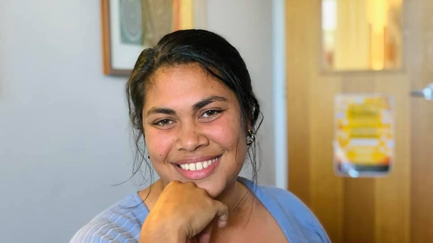 A young woman smiles at the camera with her hand on her chin