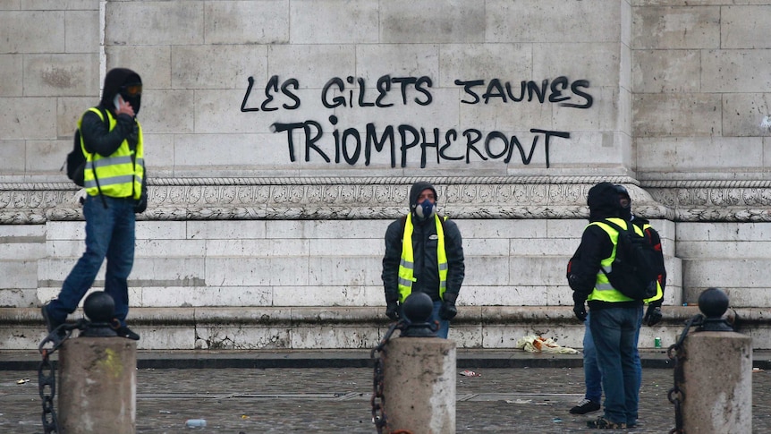 Four protesters wearing bright yellow vests stand outside the graffiti sprayed at the base of the Arc de Triomphe