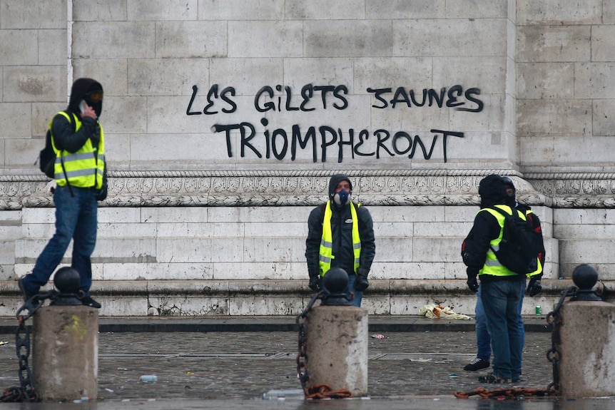 Four protesters wearing bright yellow vests stand outside the graffiti sprayed at the base of the Arc de Triomphe