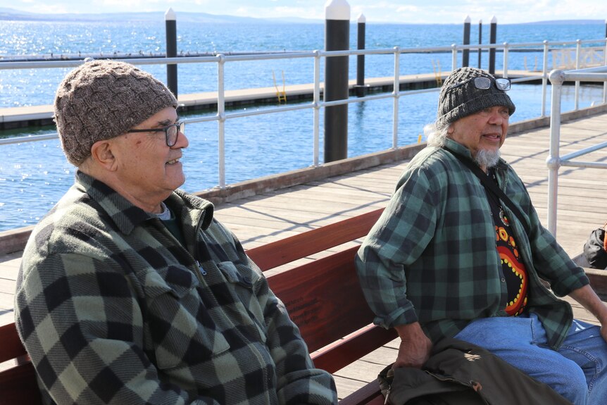 two elderly men sit on a bench on a jetty