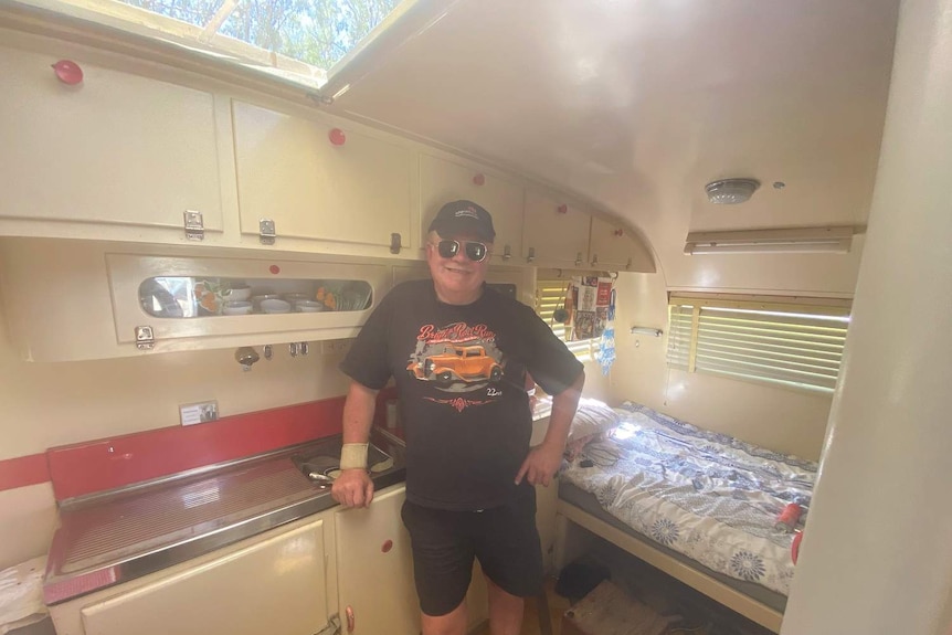 An old man standing inside an old caravan