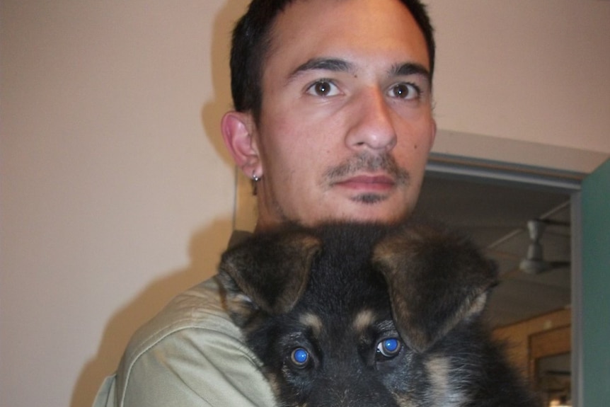 A man with dark brown hair and brown eyes holds a fluffy German Shepherd puppy