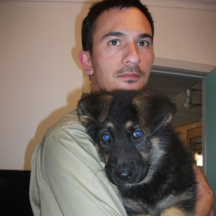 A man with dark brown hair and brown eyes holds a fluffy German Shepherd puppy