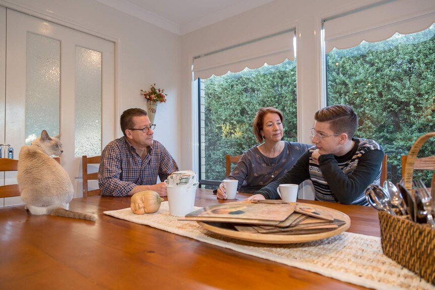 Jonah and his parents sit around their dining room table with coffee cups, talking.