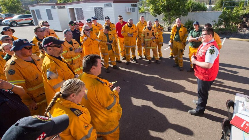 A fresh team of firefighters dressed in their suits stand in a group breifing.