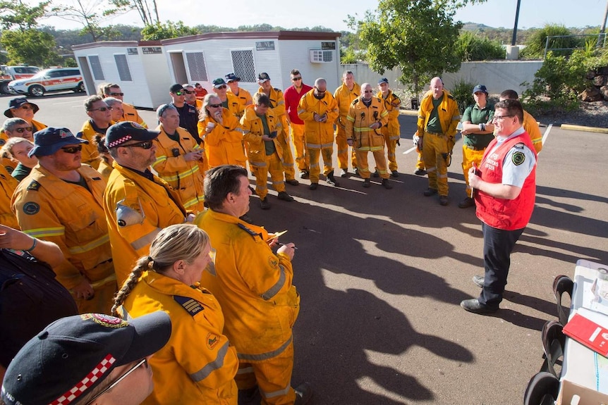 A fresh team of firefighters dressed in their suits stand in a group breifing.