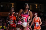 Netballer Romelda Aiken-George with ball in both hands, looking to pass, with two defenders converging