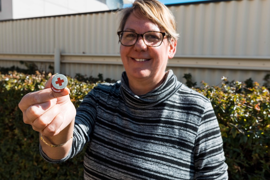 A woman holding a Red Cross badge she received for donating blood 50 times.  