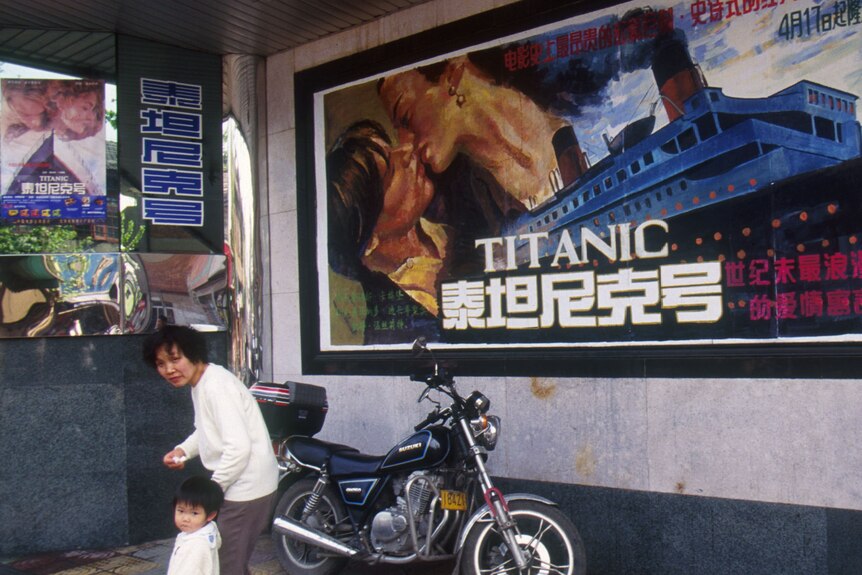 A Chinese woman and child walk past a poster for the film Titanic in English and Chinese characters