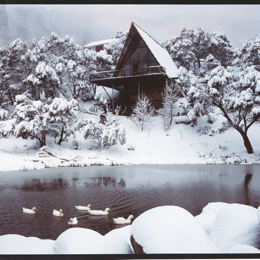 A film slide shows an a-frame building perched on a snow-covered hill overlooking a black, reflective pond.