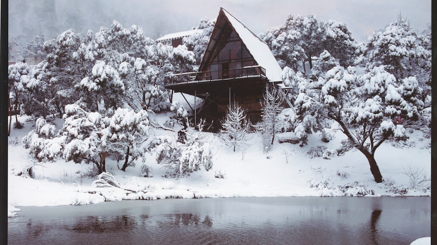 A film slide shows an a-frame building perched on a snow-covered hill overlooking a black, reflective pond.