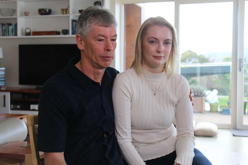 A man puts his arm around his daughter in a lounge room.