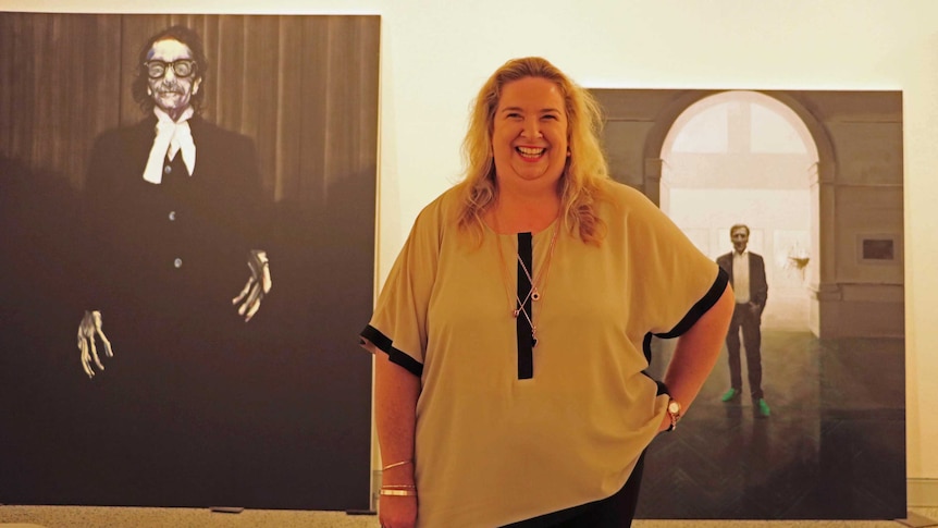 Susi Muddiman stands between Archibald Prize portraits by Nigel Milson and Tianli Zu
