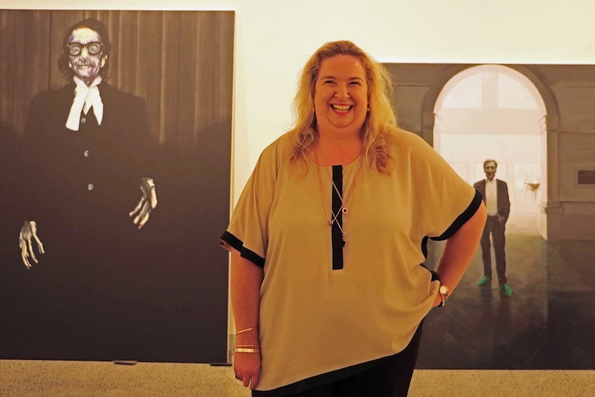 Susi Muddiman stands between Archibald Prize portraits by Nigel Milson and Tianli Zu