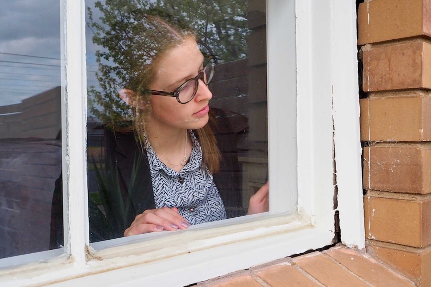 Zoe Shakallis looks through the window at a crack in the window frame.