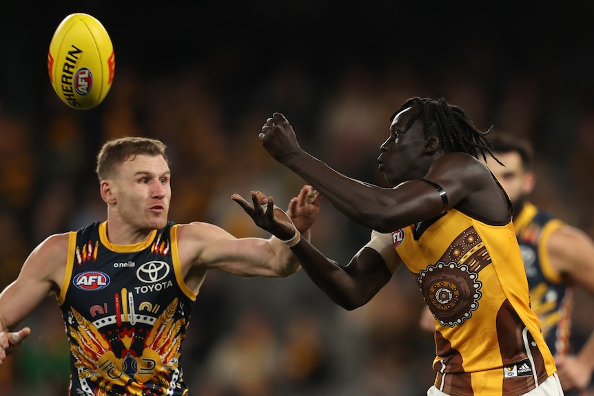 A Hawthorn defender completes a handball and the ball sails away while an Adelaide player reaches out to block.