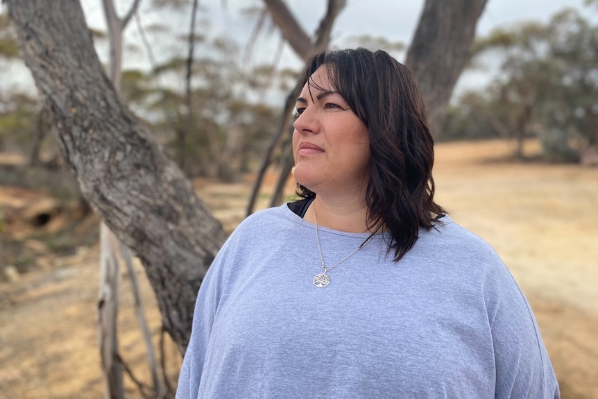 Woman standing in front of a tree looking into the distance 