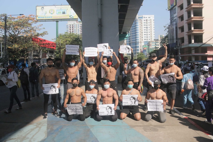 Shirtless men hold posters in Myanmar.