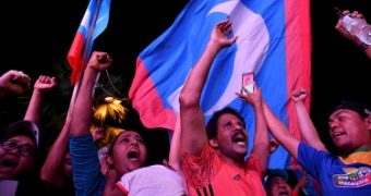 People celebrate against the backdrop of the Malaysian flag.