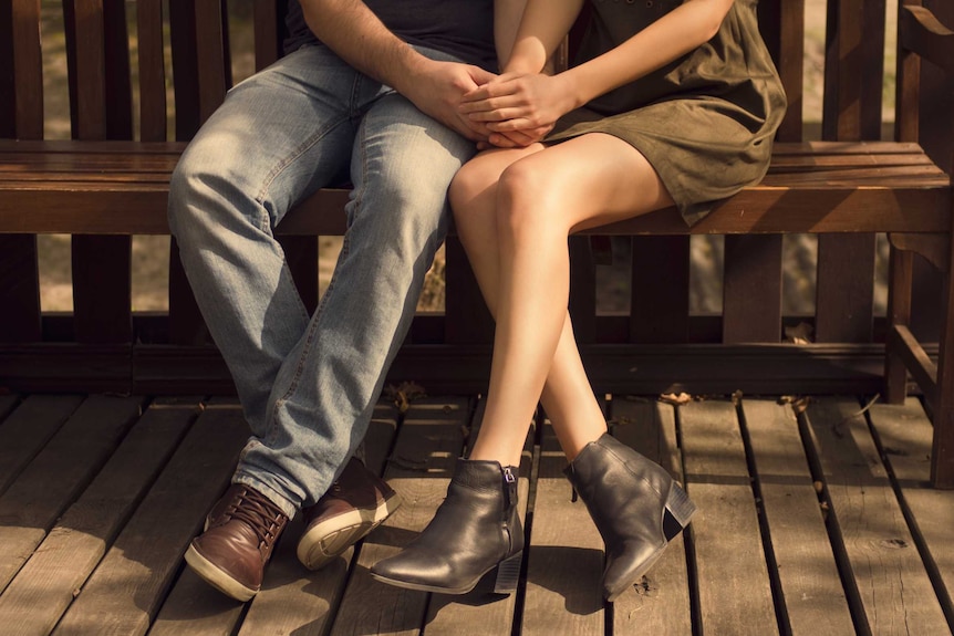 A couple holding hands on a bench.