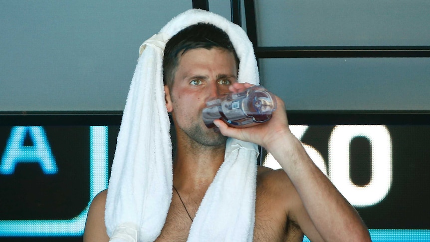 Novak Djokovic, shirtless and drinking water while sitting during a break in play.