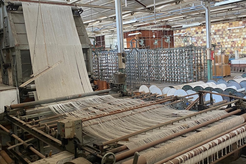 White material fed through an old textile machine inside a factory.