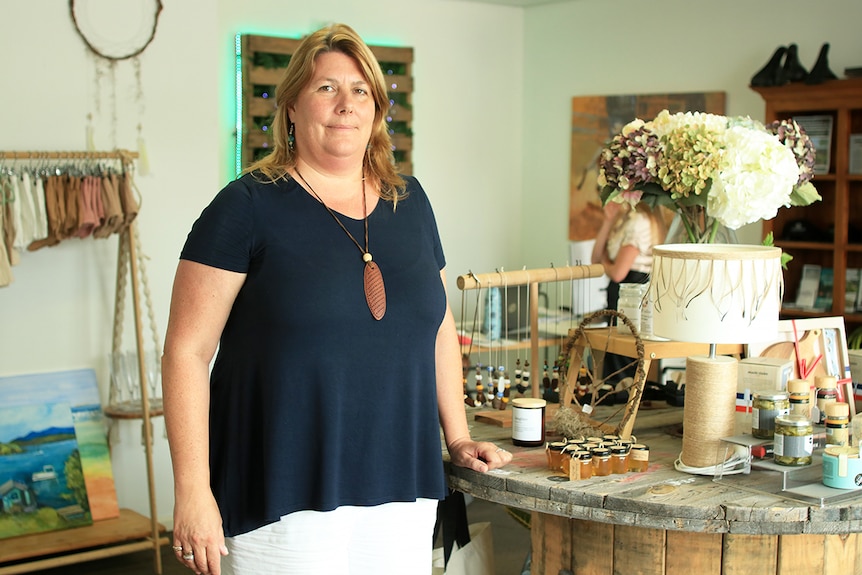 Sally Bouckley stands in her shop in Narooma with items for sale on a table.