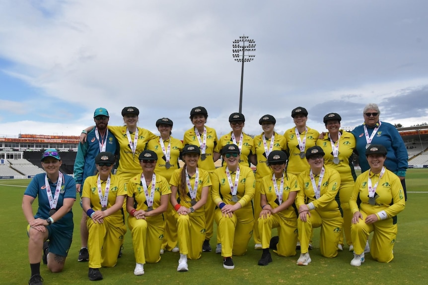 A group photo of Australia's blind women's cricket team wear their gold cricket uniform.