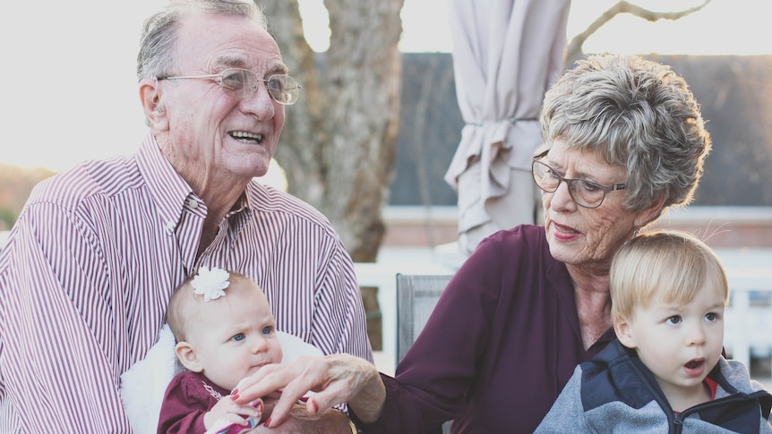 Grandfather with granddaughter on his lap sitting beside grandmother with grandson on her lap. 