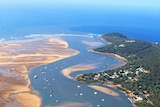 A view from the air of a river mouth with houses dotting bushland.