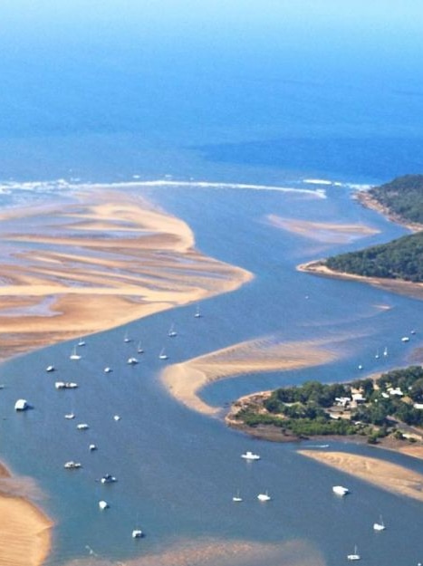 A view from the air of a river mouth with houses dotting bushland.