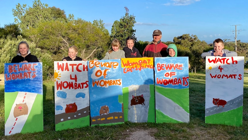 Six children stand in front of their bright, hand-painted wombat road safety signs.