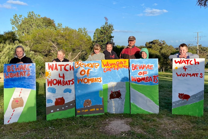 Six children stand in front of their bright, hand-painted wombat road safety signs.