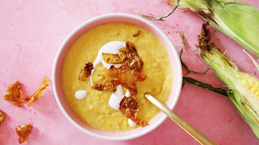 Bowl of creamy corn chowder topped with fried potato skins and coconut cream, vegetarian slow cooker meal.