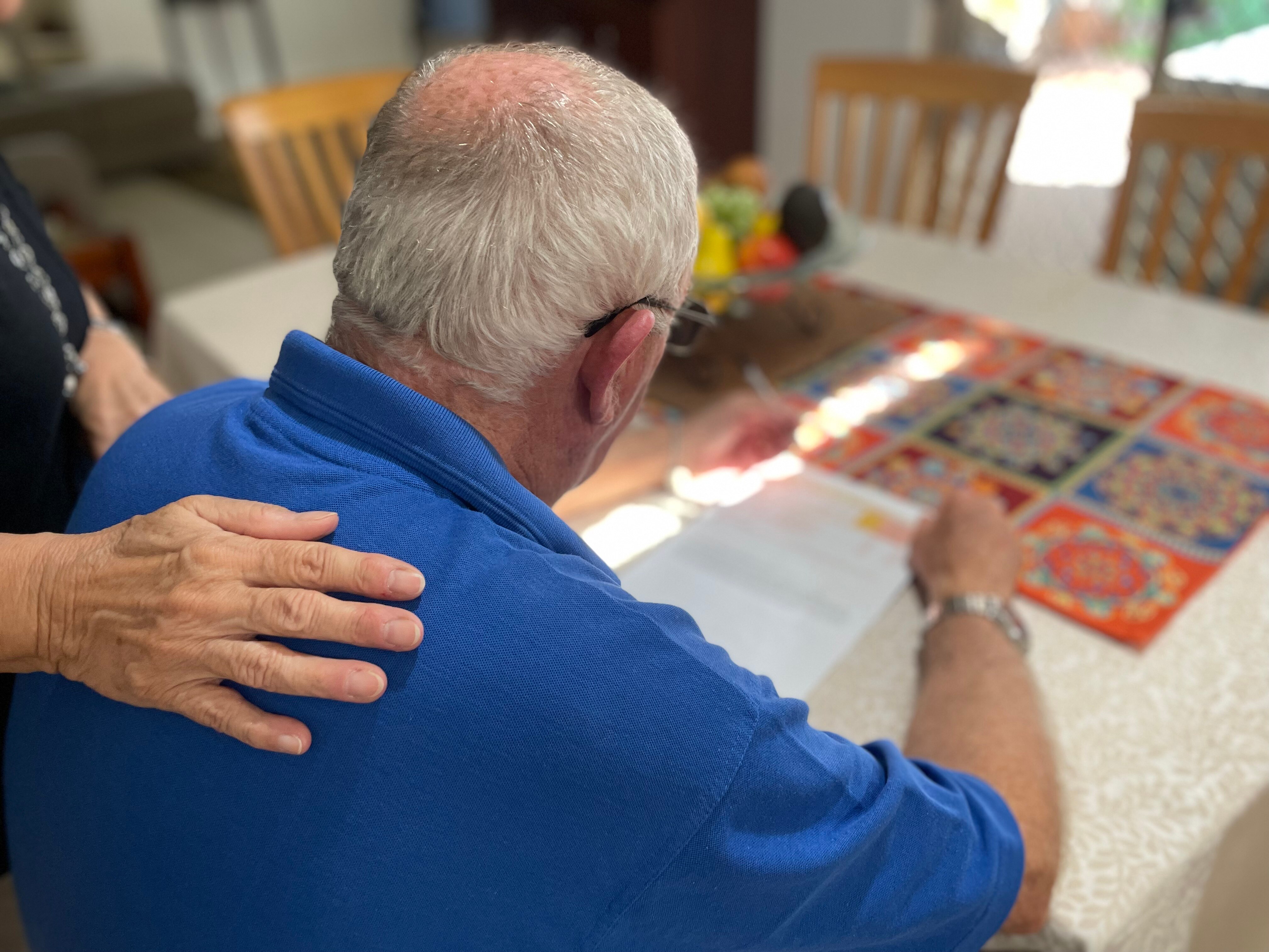A woman's hand gently lays on a man's shoulder.