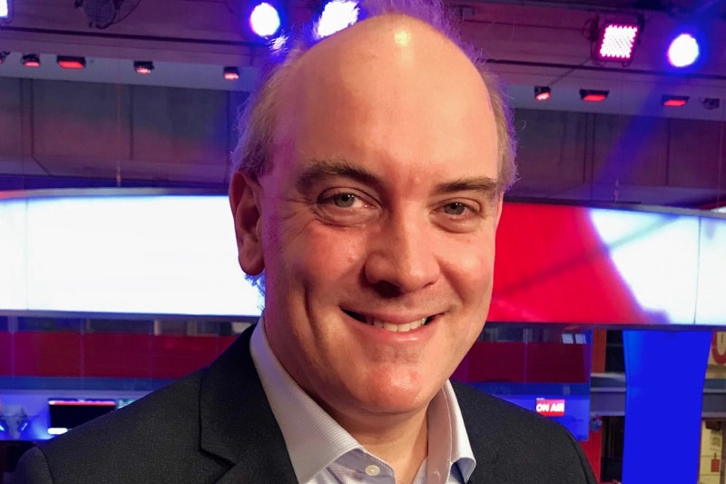 A photo of a man smiling with blue and red lights in the background.