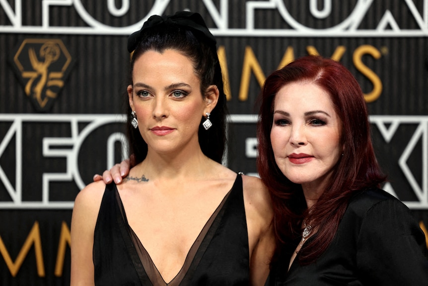 Riley Keough is pictured left with a black red carpet gown and her randmother with red hair has her arm around her