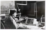 A black and white photos of a man speaking into a microphone in a studio